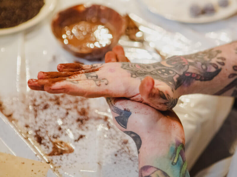 A person with tattoos on their hands is rolling a chocolate truffle